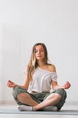 Young healthy beautiful woman practicing yoga at home sitting in lotus pose on yoga mat meditating smiling relaxed with closed eyes - Mindfulness meditation concept