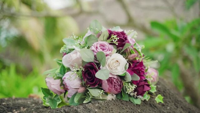 A beautiful wedding bouquet of mixed flowers laying on a stone surface outdoors
. Orbiting track shot