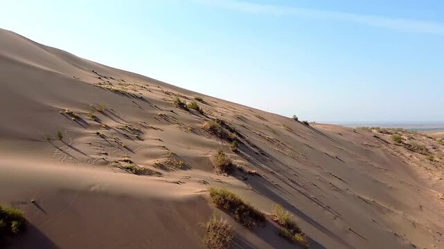 The Singing Dune is a beautiful landscape place that looks like a desert. Behind is the river. There are many bushes and traces of animals and people around. Altyn Emel, Kazakhstan. A huge sandy hill 