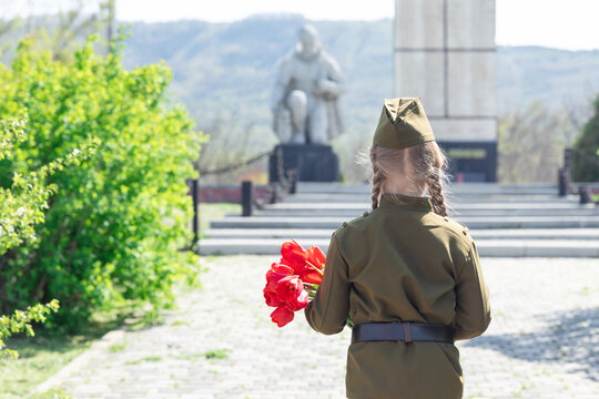 Patriotic education of youth. A girl in an old Soviet military uniform laying flowers at the monument to fallen soldiers in world War II. Victory Day