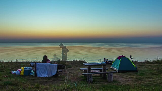 Timelapse shot of sun rising on the beach with a couple camping along the seaside during morning time. Summer trip.