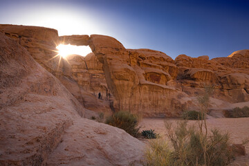 Wadi Rum w Jordanii. Słońce prześwitujące zza pustynnej formacji skalnej. - obrazy, fototapety, plakaty