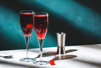 Kir Royale cocktail with black currant liqueur, prosecco wine and red cocktail cherry. Dark green background, hard light and shadow pattern