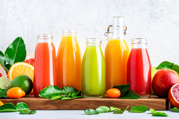 Fototapeta na wymiar Summer beverages. Citrus fruit juices, fresh and smoothies, food background. Mix of different whole and cut fruits: orange, grapefruit, lime, tangerine with leaves and bottles with drinks
