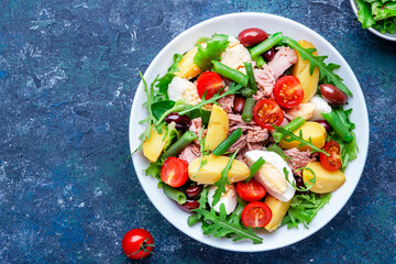 Nicoise salad with tuna, tomatoes, eggs, green beans, potatoes and olives on plate, blue table background, top view