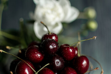 a red ripe cherry in a glass glass on a wooden table, a small white flower on a dark background
