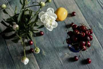 a red ripe cherry in a glass glass on a wooden table, a small white flower on a dark background