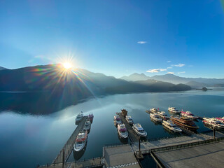 台湾　日月潭の日の出のサンビーム、山は水面に反映している。埠頭にはしけ船が数台とまっている