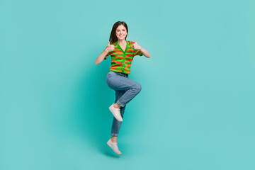 Full length photo of excited confident woman dressed striped cardigan showing two thumbs up jumping high isolated teal color background