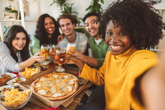 Happy group of friends making selfie drinking beer at restaurant bar - Young people having dinner sitting eating pizza - Concept of lifestyle, toasting, photo - focus on African American woman -