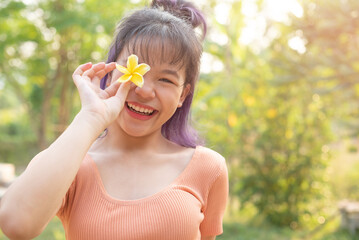 Happy teen girl 11-15 year old. Portrait of beautiful woman smiling with perfect smile at park during sunset. Girl in park smiling and covering face with flower.