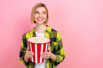 Photo portrait of pretty young girl look empty space hold popcorn bucket wear trendy plaid yellow look isolated on pink color background