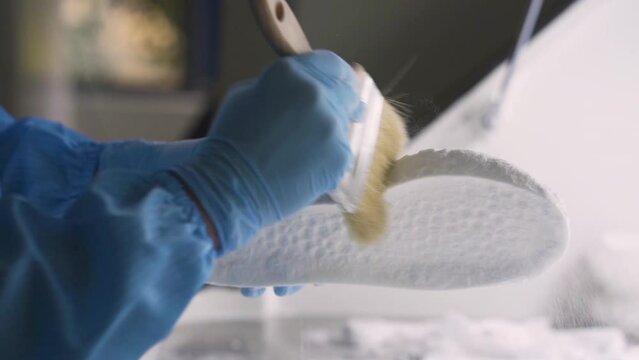 Scientist cleans 3D printed shoe sole, removing excess material and perfecting the final product.