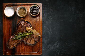 succulent grilled T-bone steak with rosemary and spices served on dark wooden board