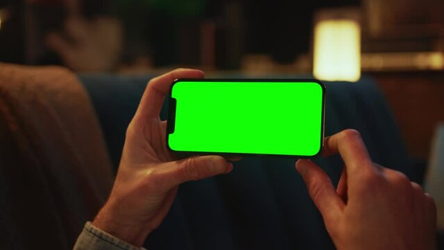 Close up hands using typing on a mobile phone with a horizontal green screen lying on a sofa. Social media. Smartphone. Mock up