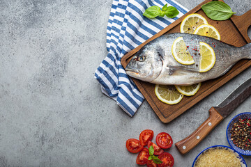 Raw fish dorado with ingredients lemon, fresh basil, cut cherry tomatoes, uncooked rice on wooden...
