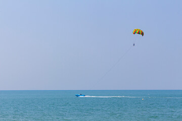 blue motorboat on horizon in Andaman Sea rolls man under parachute, shallow DOF,copy space.