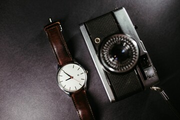 Close-up shot of a stylish wrist watch with an old retro film camera on black background
