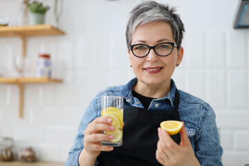 Positive smiling senior woman holding lemon and homemade lemonade in her hands.
