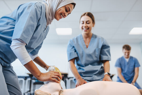 Diverse female medical students practicing CPR with an ambu bag and a mannequin in a teaching hospital