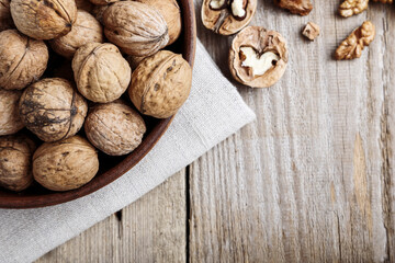 Walnut kernels in a  bowl and whole walnuts on table.