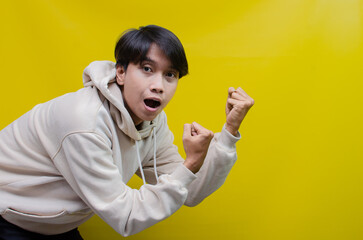 side view of an Asian man in a beige hoodie pointing his finger and opening arms to up promote and advertise something good.