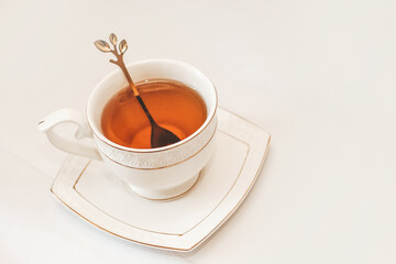 White cup with saucer and golden spoon and tea leaves.