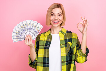 Photo portrait of attractive young woman show okey sign money fan dressed stylish checkered yellow look isolated on pink color background