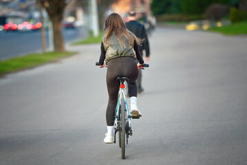 Young sporty woman in jacket and cycling tights riding bicycle in the city in spring sunny day. healthy lifestyle. Woman cycling, Slender girl ride bicycle on city street