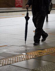 駅のホームを歩く傘を持つサラリーマンの足元