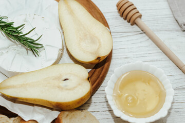 Camembert cheese with pear and rosemary sprig with honey on the table.