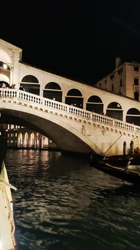 Passing under Rialto Bridge in Venice by night vertical video.