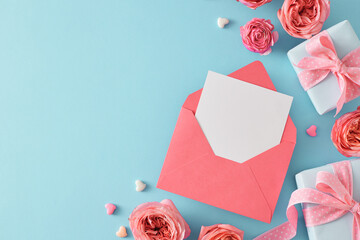 Top view photo of open envelope with white sheet pink peony rose buds gift boxes with ribbon and small hearts on light blue background with empty space. Mother Day gift concept