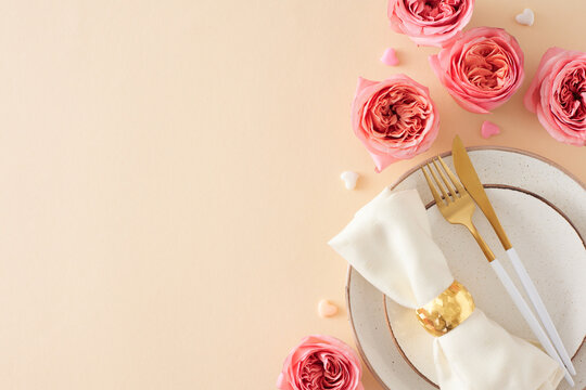 Festive setting concept for Mother's Day. Top view photo of plate cutlery knife fork napkin with ring natural flowers pink rose buds and small hearts on light beige background with empty space