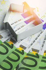 Tiny metal house and euro banknotes. Concepts of investment, paying bills or taxes.