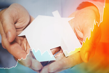 Metal house in male hands and rising sparkline chart representing real estate price or reference rate.