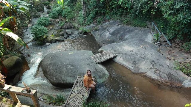 Asian fat woman Tourist stiing on bamboo bridge handmade at vacation holiday natural waterfall. Tourism travel and vacation concept
