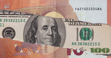 100 dollar banknote through torn Euro banknote