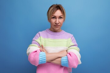 confident blond young woman in a striped sweater crossed her arms in front of her on a blue...