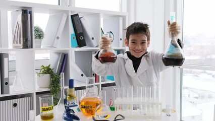 Schoolboy at chemistry lesson with dirty face showing bottles with liquids. Pupil boy happy in lab school - Powered by Adobe