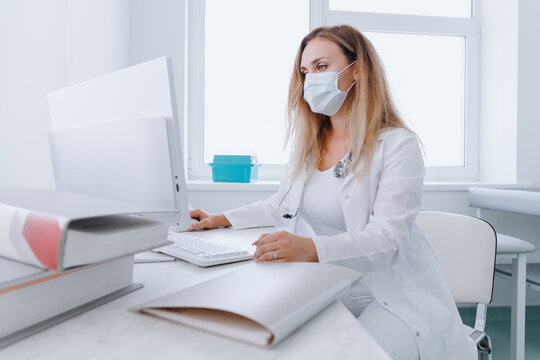 Examination in a modern clinic. A female doctor in a medical mask enters the patient's examination data into a computer.