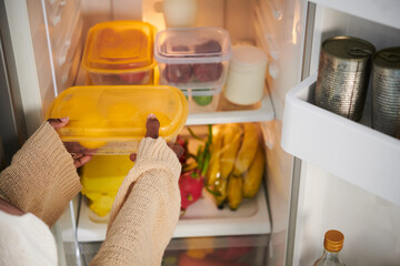 Woman taking plastic container with fresh fruits from fridge - obrazy, fototapety, plakaty