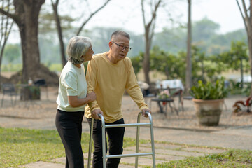 A wife helping her elderly husband patient use a walker to learn to walk. Elderly couple. Asian elderly couple giving love to each other smiling happily. Love and care for each other.