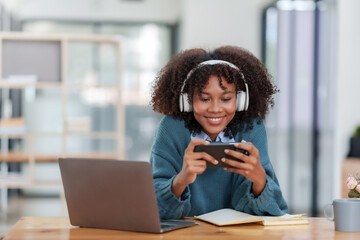 Excited young woman with curly hair wear white headphone on the head and playing games on smartphone.