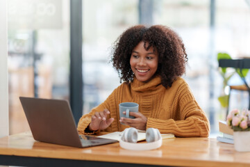 Beautiful young smiling woman with curly hair working on laptop and drinking coffee sitting at cafe.