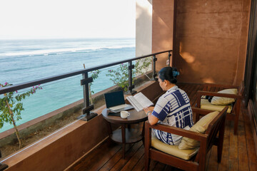 Business woman working with computer at beach resort.  Freelancer concept.  Beautiful young woman using laptop on hotel balcony with tropical beach view