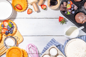 Summer baking background with baked pastry - berry cakes, muffins, mini pie tarts, with cooking baking ingredients, flour, eggs, rolling pin, cream milk, sugar, strawberry, white wooden background