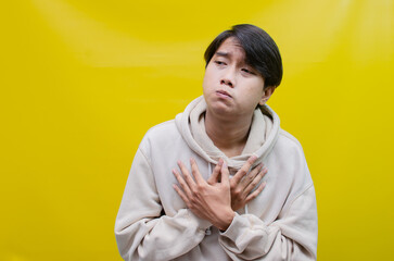 Sad A young Asian man wearing a gray t-shirt with a crying face expression is isolated over a yellow background. crying face expression of a young Asian man with a hand gesture 