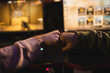 Cropped view of friends doing fist bump near blurred computers in gaming club.