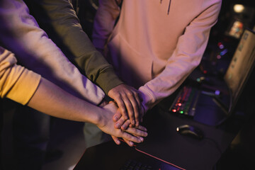 Cropped view of interracial friends holding hands in gaming club.
